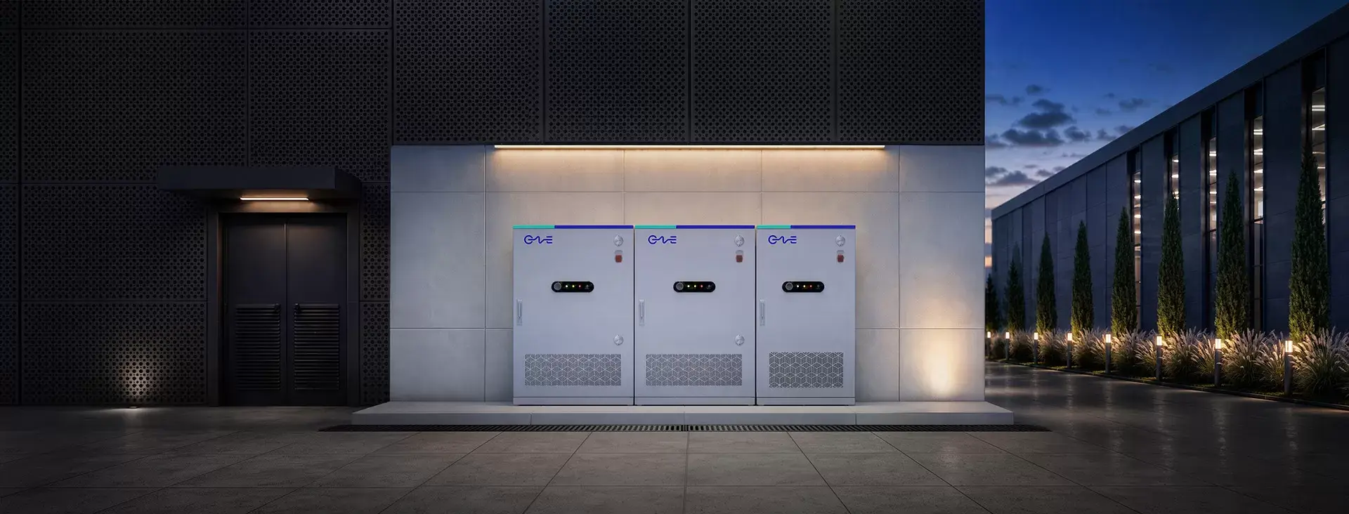 Three all-in-one battery storage cabinets installed outside a commercial building at dusk